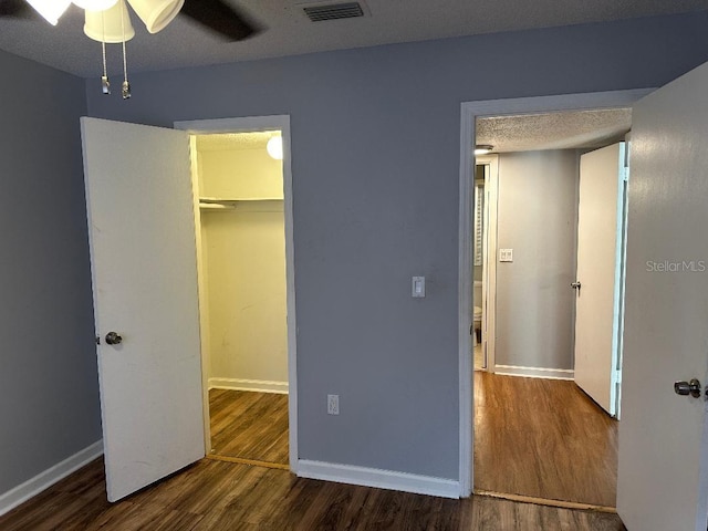 unfurnished bedroom with wood finished floors, baseboards, a walk in closet, a closet, and a textured ceiling