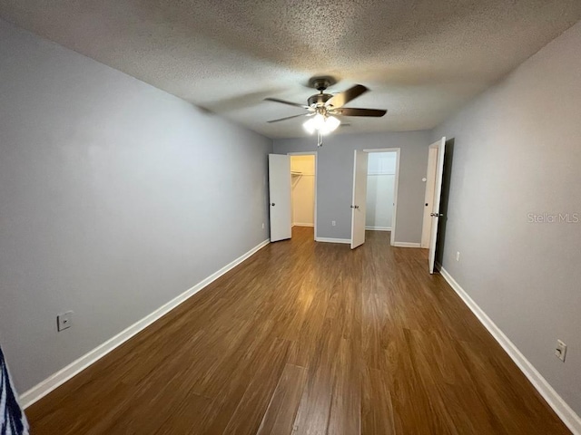 unfurnished bedroom featuring dark wood-type flooring, baseboards, a walk in closet, a textured ceiling, and a ceiling fan