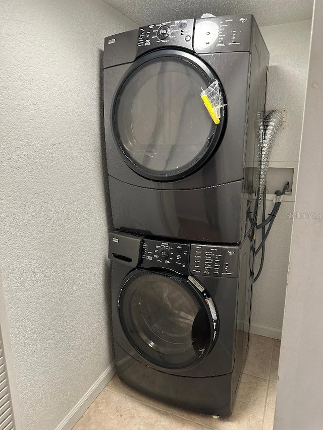 washroom featuring stacked washer / dryer, a textured wall, baseboards, and tile patterned floors