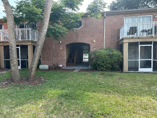rear view of property with brick siding, a yard, and a balcony