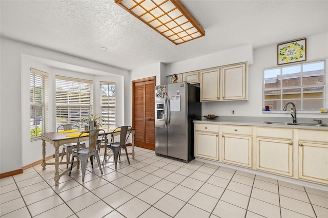 kitchen featuring cream cabinets, stainless steel refrigerator with ice dispenser, a sink, a textured ceiling, and baseboards