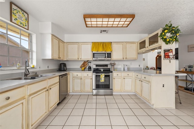 kitchen with appliances with stainless steel finishes, cream cabinets, a sink, a peninsula, and a textured ceiling