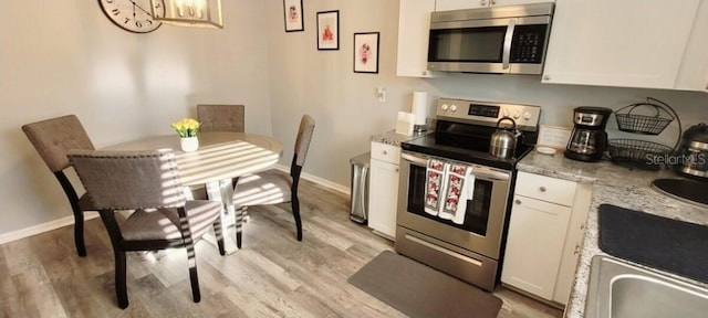2729 Club Cortile Cir, Kissimmee, FL 34746 - kitchen with appliances with stainless steel finishes, white cabinetry, light wood-style flooring, and baseboards