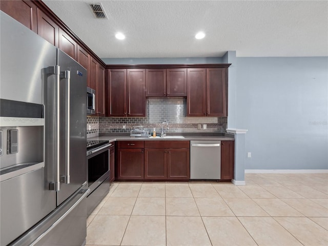 kitchen with appliances with stainless steel finishes, decorative backsplash, light tile patterned floors, a sink, and a textured ceiling