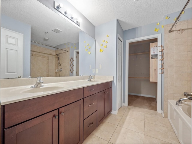 full bath with tile patterned flooring, a textured ceiling, double vanity, and a walk in closet