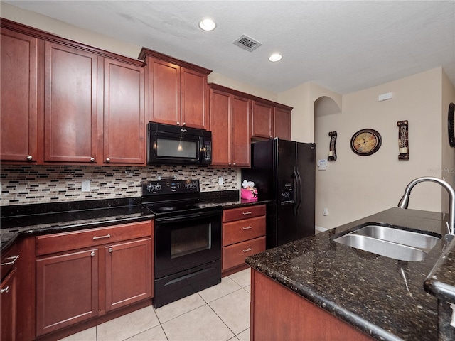 kitchen featuring black appliances, a sink, light tile patterned floors, backsplash, and dark stone counters