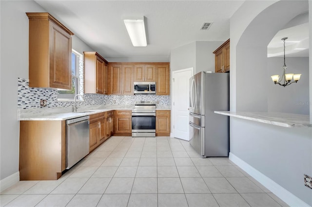 5768 Los Palma Vista Dr, Orlando, FL 32837 - kitchen with stainless steel appliances, decorative backsplash, a chandelier, a sink, and brown cabinets