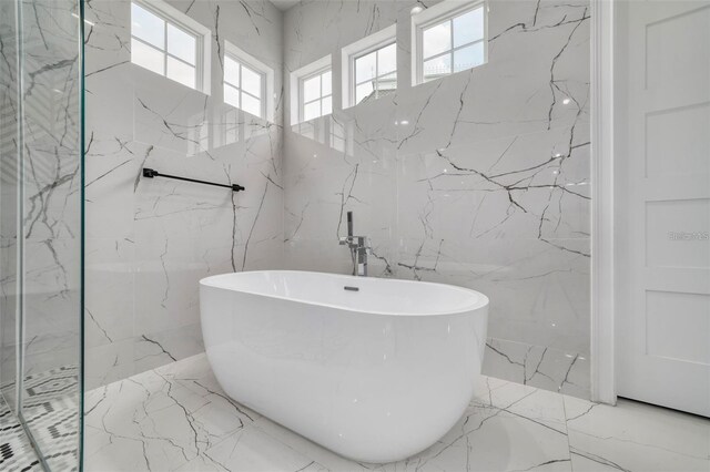 423 Arbor Cir, Celebration, FL 34747 - bathroom featuring marble tiled floors, tile walls, plenty of natural light, a soaking tub, and stone wall