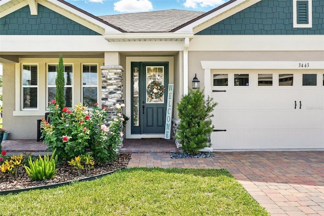 property entrance with stucco siding, covered porch, a garage, driveway, and roof with shingles