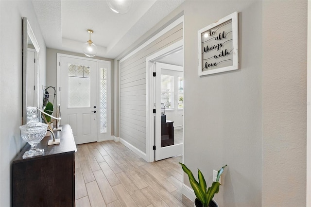 foyer entrance featuring baseboards, light wood-type flooring, and a raised ceiling