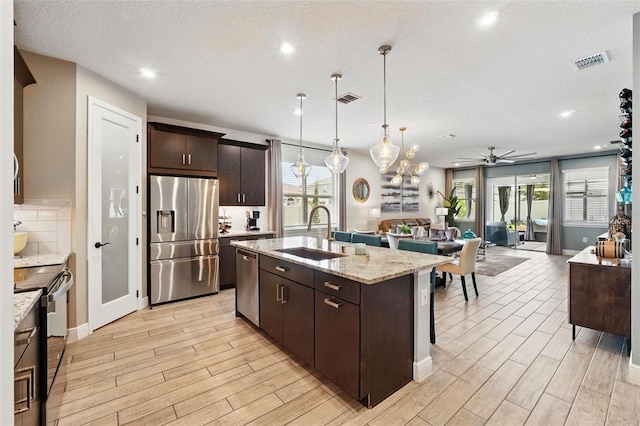 kitchen featuring stainless steel appliances, a sink, open floor plan, a ceiling fan, and dark brown cabinetry