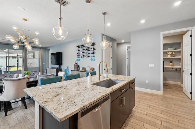 kitchen with dishwasher, a sink, light wood-style floors, an island with sink, and decorative light fixtures