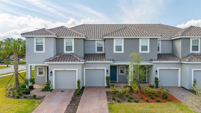 view of property featuring driveway, a tile roof, an attached garage, and stucco siding