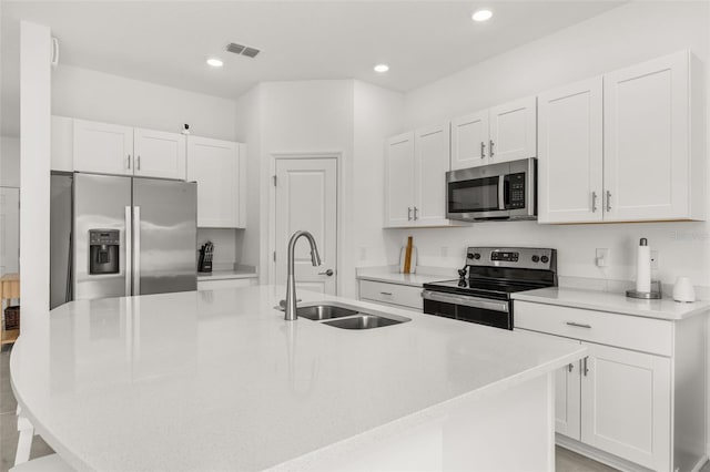kitchen with appliances with stainless steel finishes, a sink, a kitchen island with sink, white cabinets, and recessed lighting