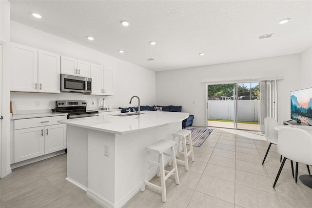 kitchen featuring appliances with stainless steel finishes, a sink, white cabinetry, a center island with sink, and a textured ceiling