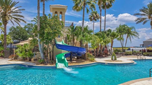 community pool featuring fence and a water slide
