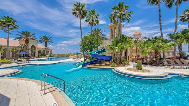 community pool with a water slide, fence, and a patio