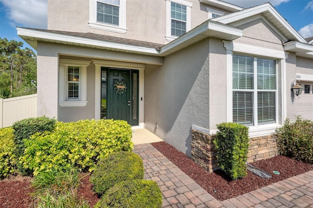 entrance to property with stucco siding, fence, and stone siding