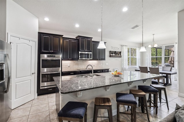 kitchen featuring appliances with stainless steel finishes, a sink, a kitchen bar, decorative backsplash, and dark stone countertops