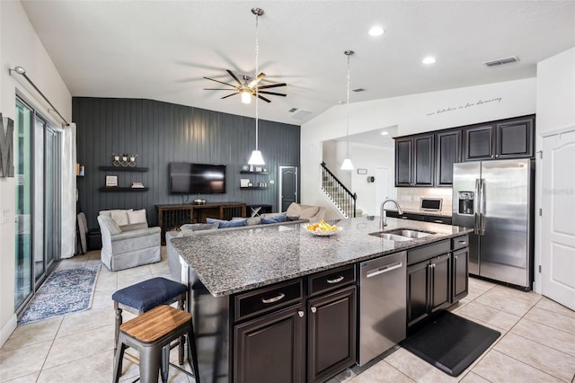 kitchen featuring appliances with stainless steel finishes, a sink, light tile patterned flooring, stone countertops, and vaulted ceiling