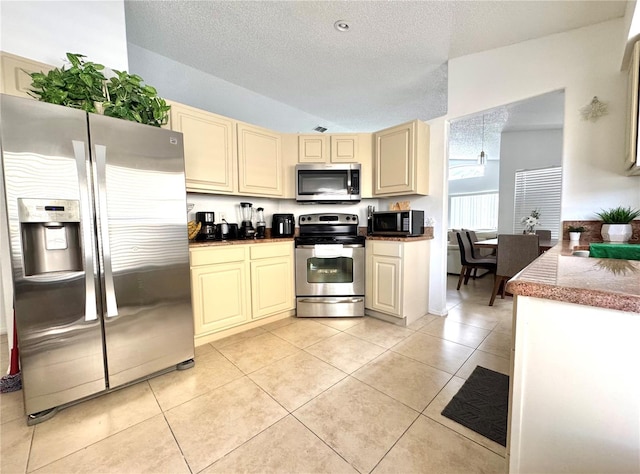kitchen with appliances with stainless steel finishes, cream cabinetry, a textured ceiling, light tile patterned floors, and vaulted ceiling