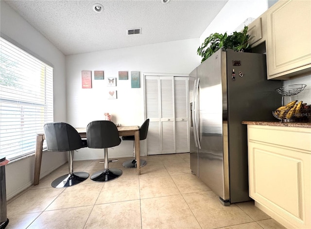 kitchen featuring stainless steel refrigerator with ice dispenser, cream cabinets, a textured ceiling, and light tile patterned flooring