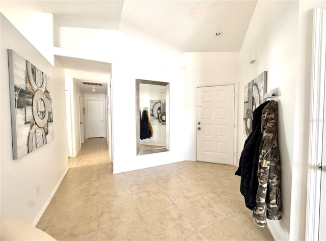 hallway with light tile patterned floors, lofted ceiling, a textured ceiling, and baseboards