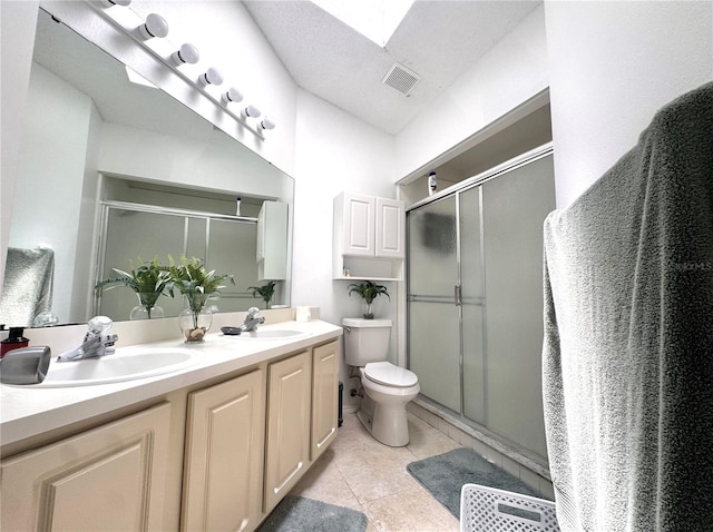 bathroom with a stall shower, toilet, double vanity, and tile patterned flooring