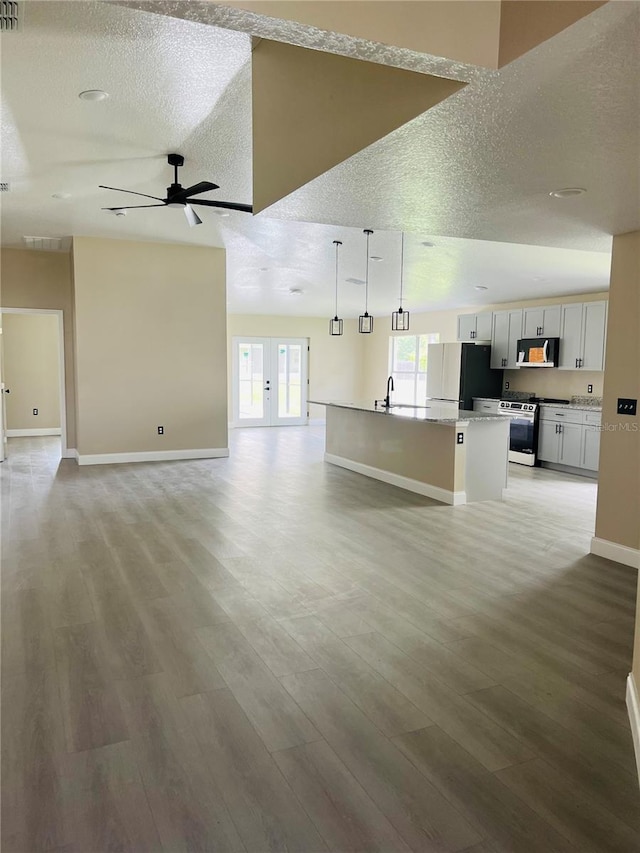 unfurnished living room featuring ceiling fan, baseboards, light wood finished floors, a sink, and french doors