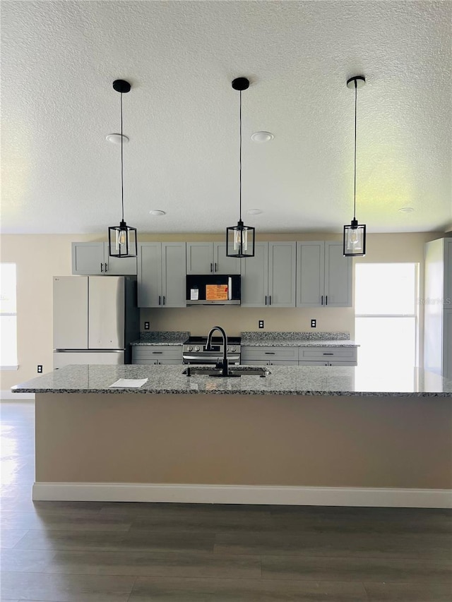 kitchen featuring stainless steel microwave, a sink, freestanding refrigerator, a textured ceiling, and dark wood finished floors