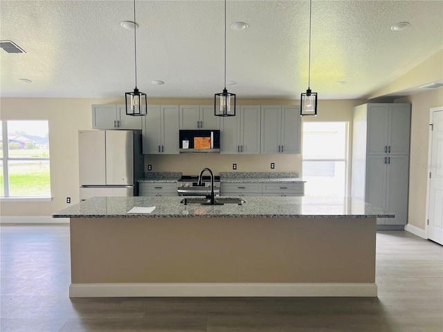 kitchen featuring stainless steel appliances, a textured ceiling, light wood-style floors, baseboards, and a kitchen island with sink