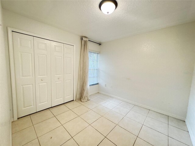 2330 Prime Cir Unit A, Kissimmee, FL 34746 - unfurnished bedroom with a textured ceiling, light tile patterned flooring, a closet, and baseboards