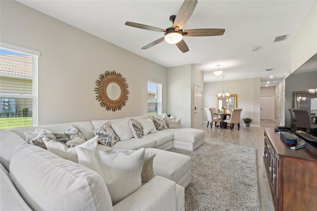 living area with a chandelier, light wood-type flooring, a ceiling fan, and baseboards