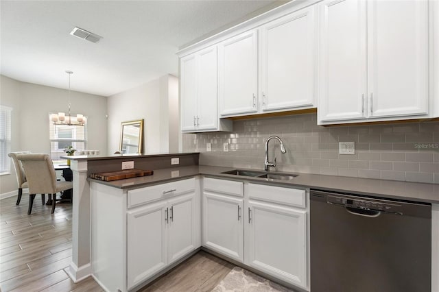 kitchen featuring dishwashing machine, a sink, a chandelier, a peninsula, and backsplash