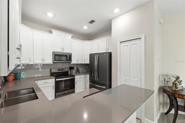 kitchen with stainless steel appliances, backsplash, white cabinets, a sink, and recessed lighting