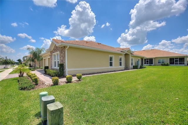 rear view of property featuring a tiled roof, stucco siding, a yard, and stone siding
