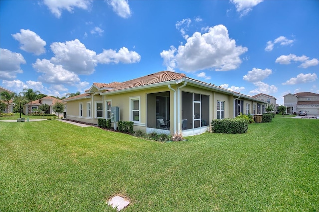 rear view of house with a yard, stucco siding, a tiled roof, and a sunroom