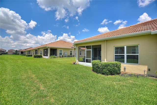 back of house featuring stucco siding, a lawn, a sunroom, and a tile roof