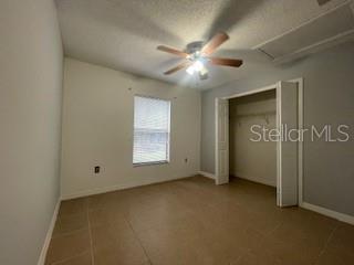 116 Talavera Ln, Kissimmee, FL 34758 - unfurnished bedroom featuring baseboards, attic access, ceiling fan, a textured ceiling, and tile patterned flooring