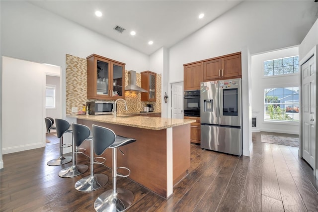 149 Imperial Oak Ct, Davenport, FL 33896 - kitchen featuring appliances with stainless steel finishes, wall chimney range hood, high vaulted ceiling, light stone counters, and brown cabinetry