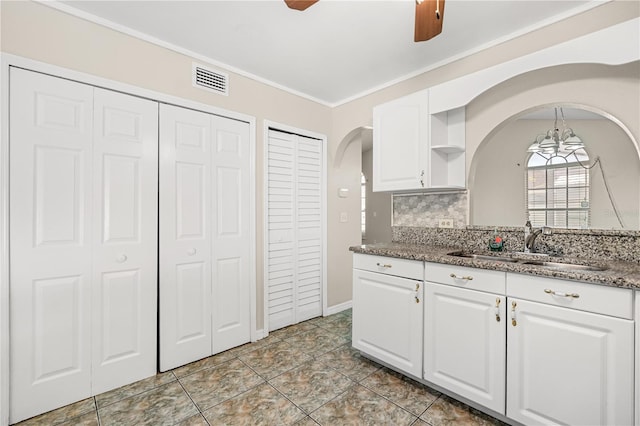 kitchen with arched walkways, a sink, white cabinets, backsplash, and a chandelier