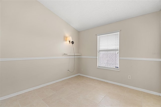 spare room featuring lofted ceiling, baseboards, light tile patterned floors, and a textured ceiling