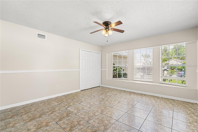 tiled empty room with a textured ceiling, ceiling fan, and baseboards