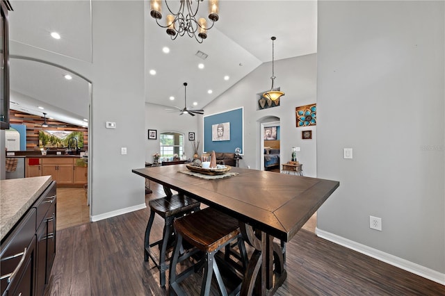dining room featuring arched walkways, dark wood-type flooring, baseboards, high vaulted ceiling, and a chandelier