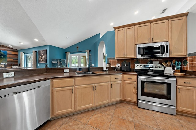 kitchen with appliances with stainless steel finishes, a sink, lofted ceiling, dark countertops, and arched walkways