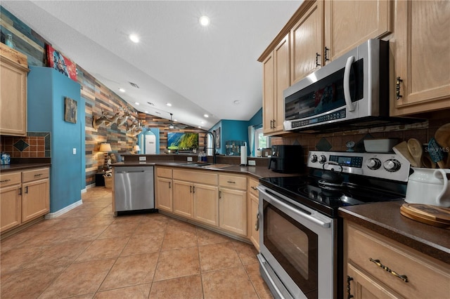 kitchen featuring appliances with stainless steel finishes, a sink, vaulted ceiling, dark countertops, and a peninsula