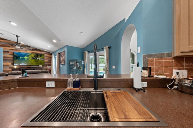 kitchen with lofted ceiling, dark countertops, open floor plan, arched walkways, and a textured ceiling