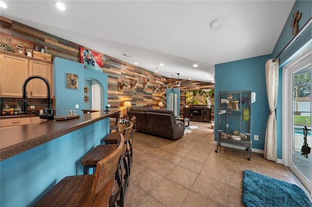 living room with arched walkways, an accent wall, wood walls, recessed lighting, and light tile patterned floors