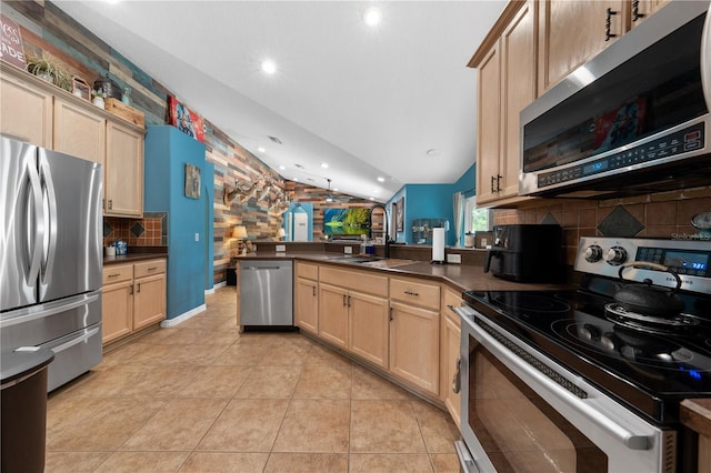 kitchen with appliances with stainless steel finishes, a peninsula, vaulted ceiling, tasteful backsplash, and dark countertops