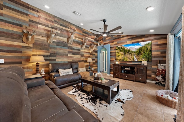 tiled living area with wooden walls, a textured ceiling, recessed lighting, ceiling fan, and arched walkways